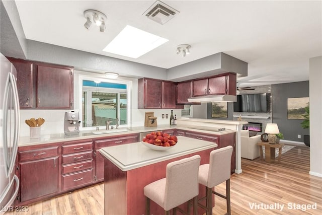 kitchen featuring visible vents, a kitchen island, a sink, dark brown cabinets, and a kitchen bar