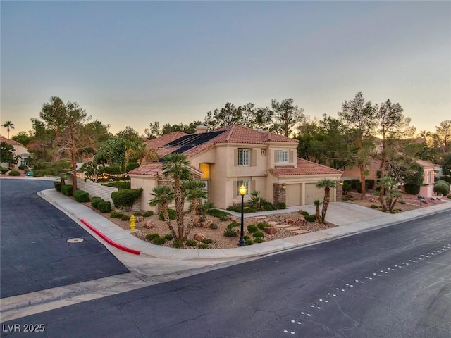 mediterranean / spanish-style home with driveway, a garage, solar panels, a tiled roof, and stucco siding