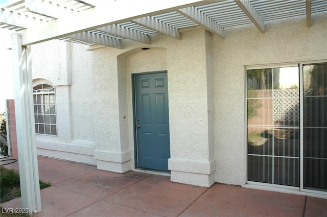 view of exterior entry featuring a pergola and stucco siding