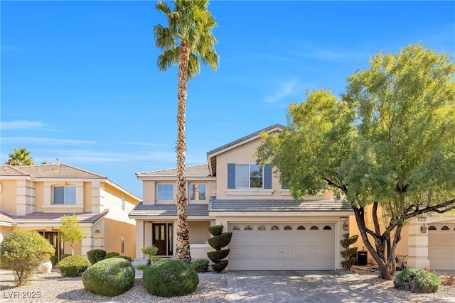 view of front of house featuring decorative driveway, a tile roof, an attached garage, and stucco siding