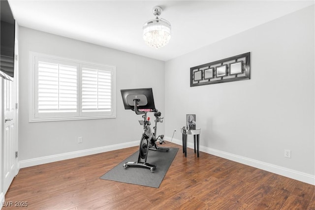 workout area featuring a chandelier, dark wood finished floors, and baseboards