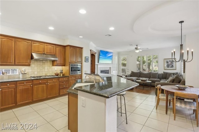 kitchen with decorative light fixtures, open floor plan, dark stone countertops, an island with sink, and under cabinet range hood