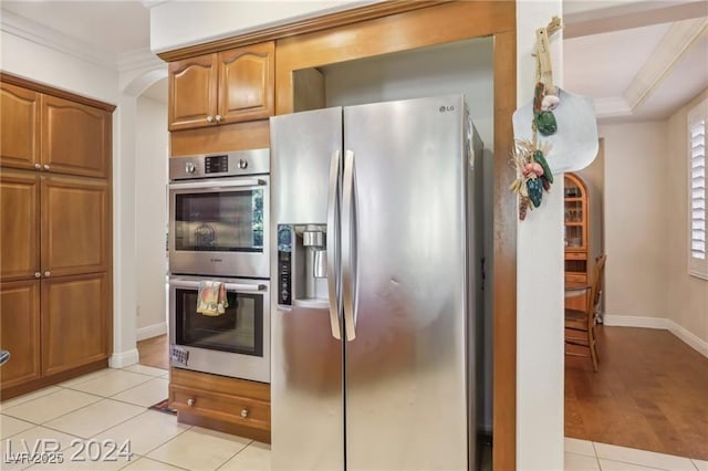kitchen featuring appliances with stainless steel finishes, light tile patterned flooring, brown cabinets, and crown molding