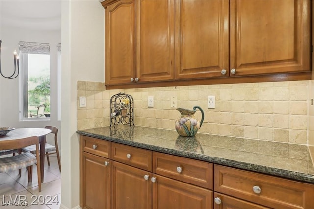 kitchen with brown cabinets, tasteful backsplash, dark stone counters, and light tile patterned flooring
