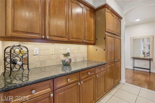 kitchen with light tile patterned floors, baseboards, brown cabinetry, dark stone counters, and backsplash