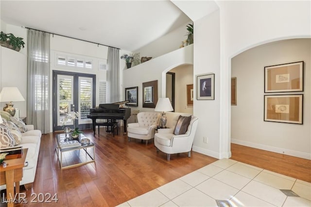 living area with arched walkways, french doors, light wood-style flooring, and a towering ceiling