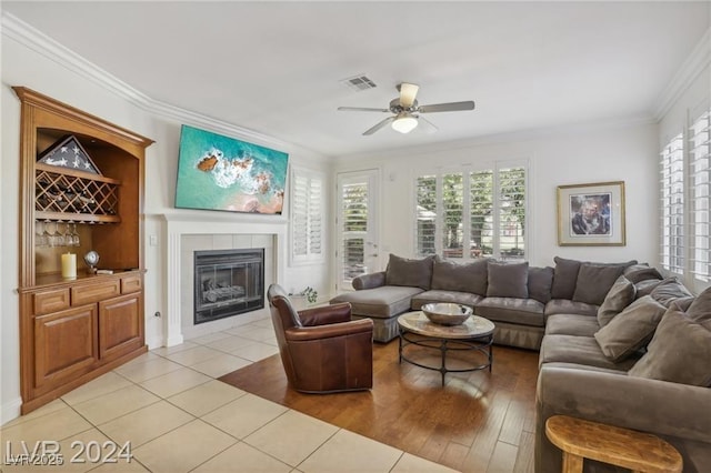 living area with a fireplace, light tile patterned floors, visible vents, ornamental molding, and a ceiling fan