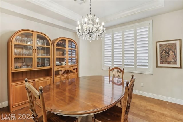 dining area featuring a tray ceiling, crown molding, a chandelier, light wood-type flooring, and baseboards