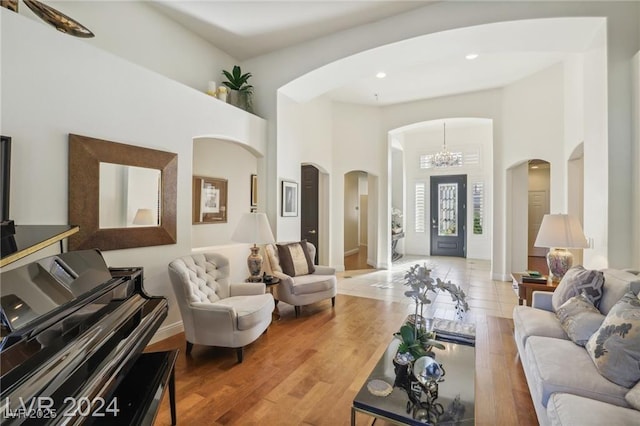 living room featuring light wood-type flooring, arched walkways, a high ceiling, and an inviting chandelier