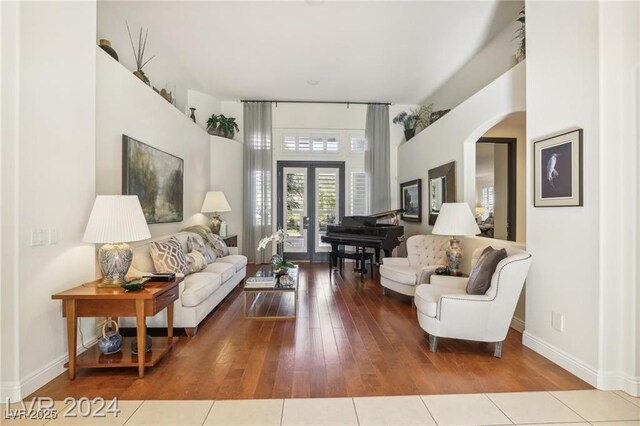 living room with arched walkways, french doors, light wood-style flooring, and baseboards