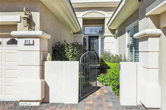 doorway to property with a garage, a gate, and stucco siding