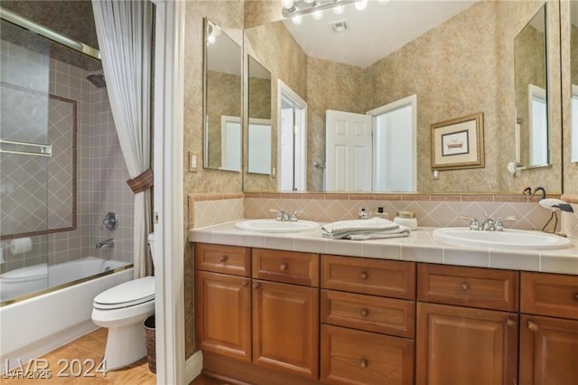 full bathroom with double vanity, visible vents, toilet, combined bath / shower with glass door, and a sink