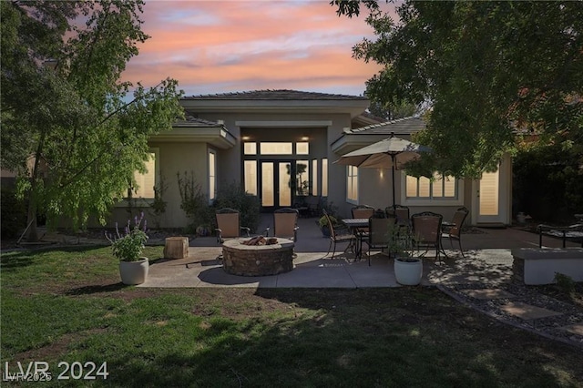 rear view of property featuring a yard, a patio, an outdoor fire pit, and stucco siding
