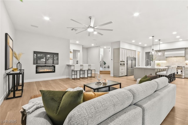 living area with light wood finished floors, recessed lighting, a glass covered fireplace, ceiling fan, and baseboards