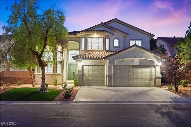 mediterranean / spanish-style house with a garage, driveway, a tiled roof, and stucco siding