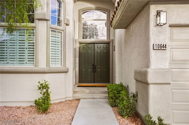 view of exterior entry featuring a garage and stucco siding