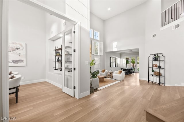 entrance foyer featuring baseboards, visible vents, light wood-style flooring, and a high ceiling