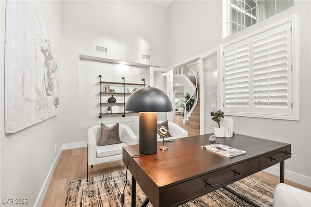 home office with baseboards, visible vents, light wood-style flooring, and a high ceiling