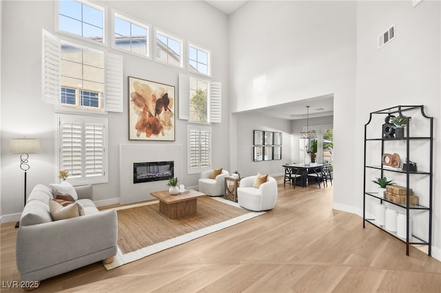 living area with light wood-style floors, plenty of natural light, visible vents, and a glass covered fireplace