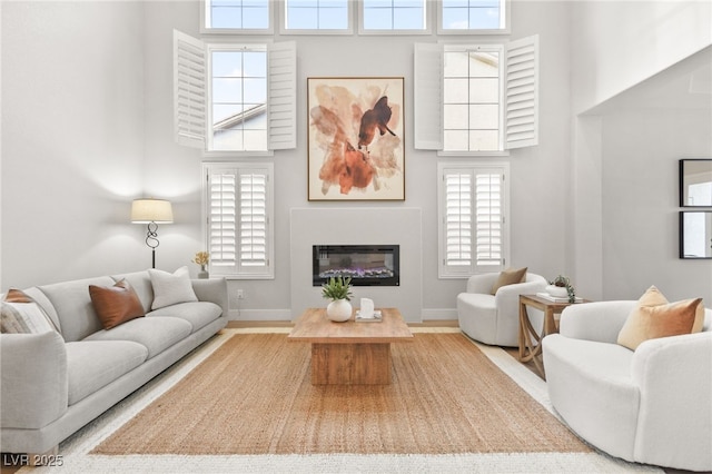 living area with plenty of natural light, a glass covered fireplace, and a towering ceiling