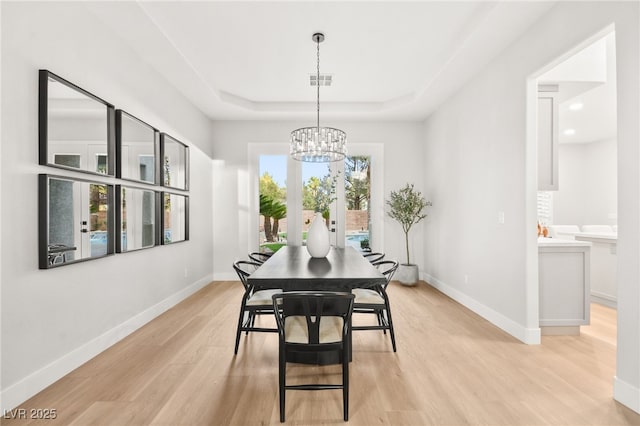 dining space with light wood finished floors, baseboards, a tray ceiling, and an inviting chandelier