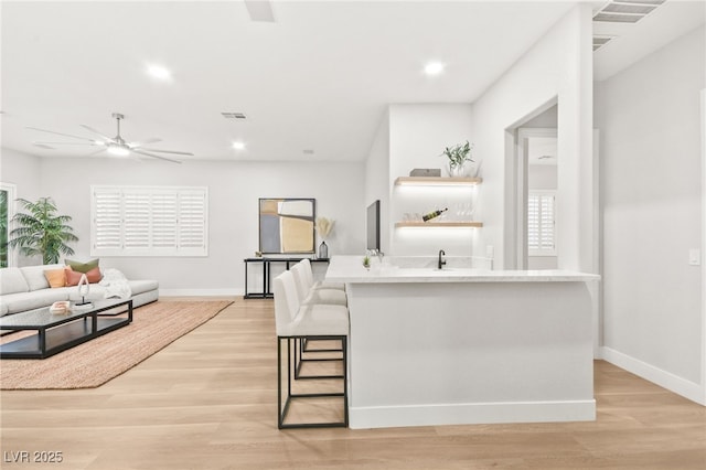 kitchen featuring an island with sink, light wood-style floors, visible vents, and open floor plan