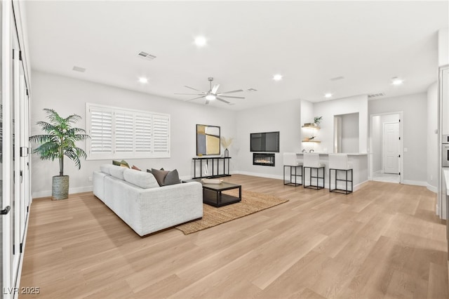 living room with light wood finished floors, visible vents, baseboards, a glass covered fireplace, and recessed lighting