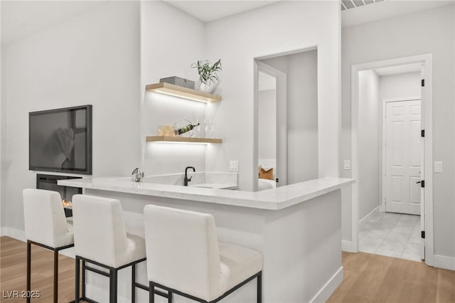 bar featuring light wood finished floors, baseboards, and indoor wet bar