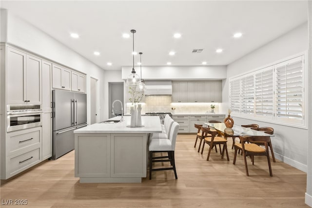 kitchen with light countertops, gray cabinetry, appliances with stainless steel finishes, a sink, and an island with sink