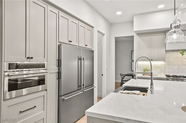 kitchen with decorative backsplash, decorative light fixtures, light stone countertops, stainless steel appliances, and a sink