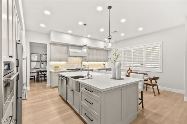 kitchen featuring visible vents, a kitchen island with sink, light countertops, premium range hood, and pendant lighting