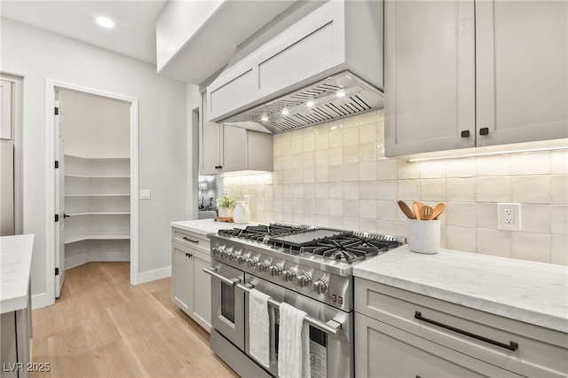 kitchen featuring light wood-style flooring, custom range hood, light stone counters, double oven range, and backsplash