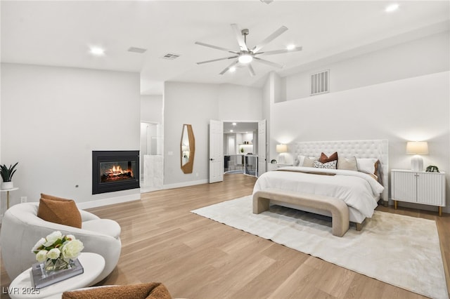 bedroom featuring light wood-style floors, visible vents, vaulted ceiling, and a glass covered fireplace