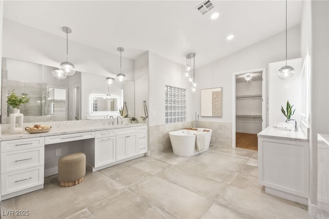 full bathroom with tile walls, lofted ceiling, a soaking tub, visible vents, and vanity