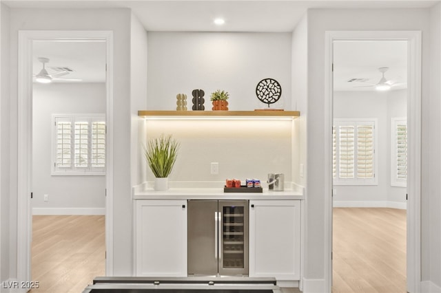 bar with beverage cooler, ceiling fan, light wood-type flooring, and baseboards