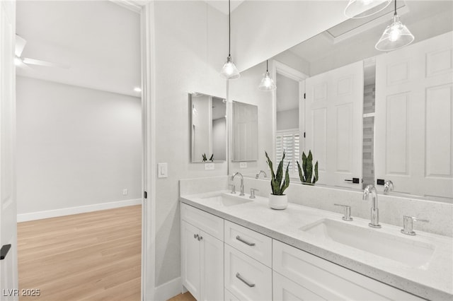 full bathroom featuring double vanity, a sink, baseboards, and wood finished floors