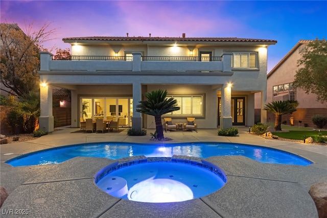 back of property featuring stucco siding, a pool with connected hot tub, outdoor dining space, a patio area, and a balcony