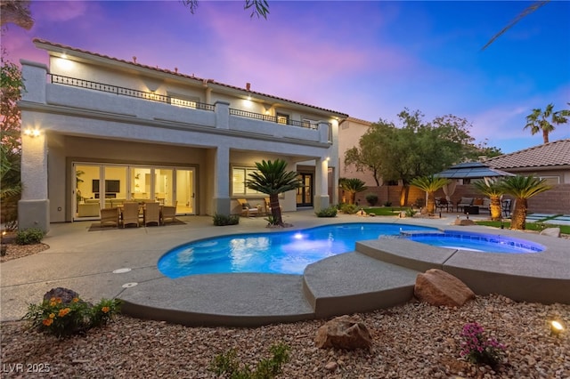 pool at dusk with a patio, fence, a pool with connected hot tub, a gazebo, and outdoor dining space