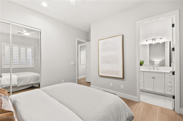 bedroom featuring a sink, baseboards, a closet, light wood finished floors, and ensuite bath