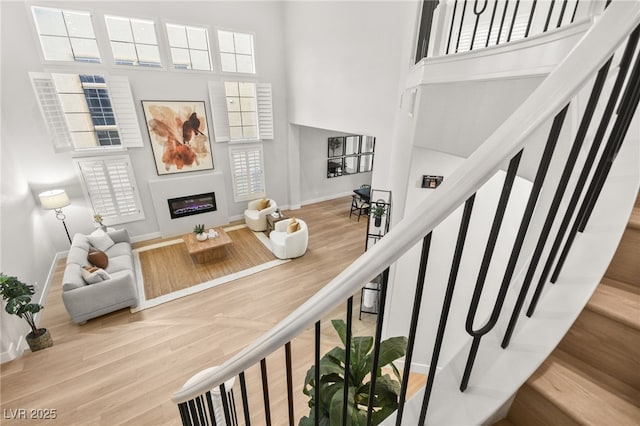 interior space with a glass covered fireplace, baseboards, a high ceiling, and wood finished floors