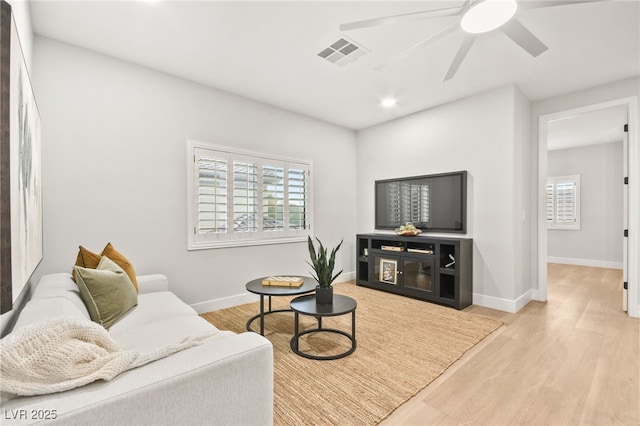 living room featuring baseboards, ceiling fan, visible vents, and light wood-style floors