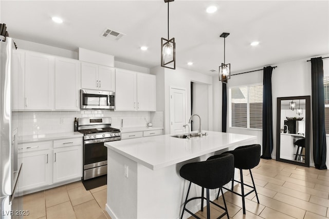 kitchen with light countertops, hanging light fixtures, appliances with stainless steel finishes, white cabinets, and an island with sink