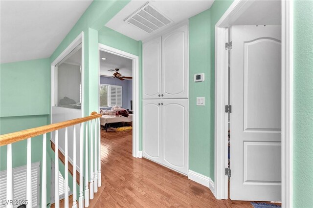 hallway with visible vents, light wood-style flooring, and baseboards