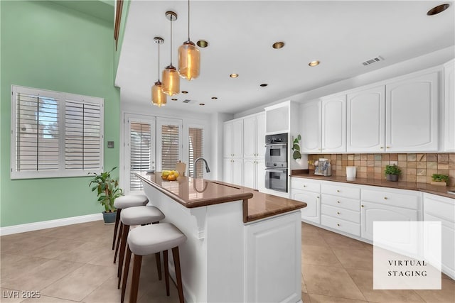 8629 Estrelita Dr, Las Vegas, NV 89128 - kitchen with dark countertops, stainless steel double oven, light tile patterned flooring, backsplash, and a kitchen bar