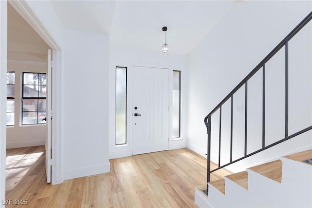 entryway with light wood-style flooring, baseboards, and stairs