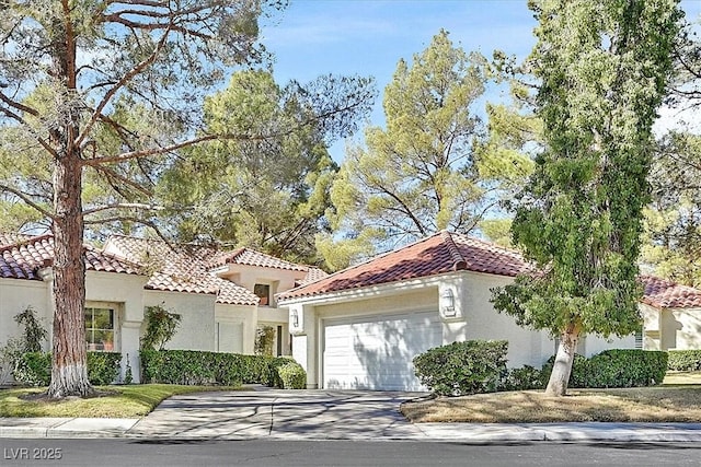 mediterranean / spanish house with an attached garage, a tile roof, concrete driveway, and stucco siding