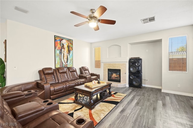 living room featuring a fireplace, visible vents, ceiling fan, wood finished floors, and baseboards