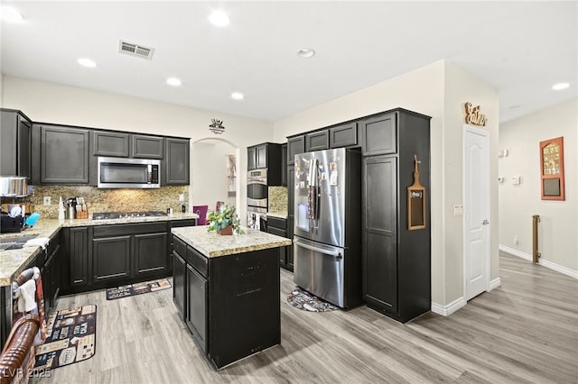 kitchen with stainless steel appliances, a center island, dark cabinetry, and light stone counters