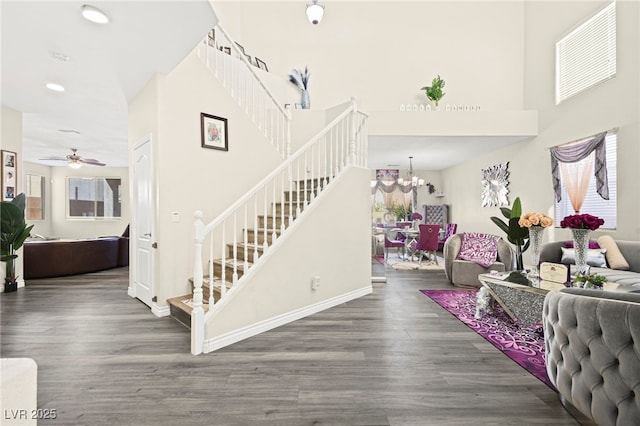 interior space featuring recessed lighting, a towering ceiling, wood finished floors, baseboards, and ceiling fan with notable chandelier