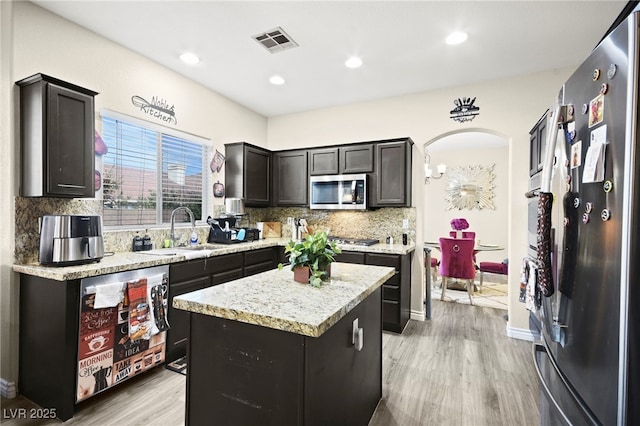 kitchen with arched walkways, visible vents, a kitchen island, stainless steel appliances, and a sink